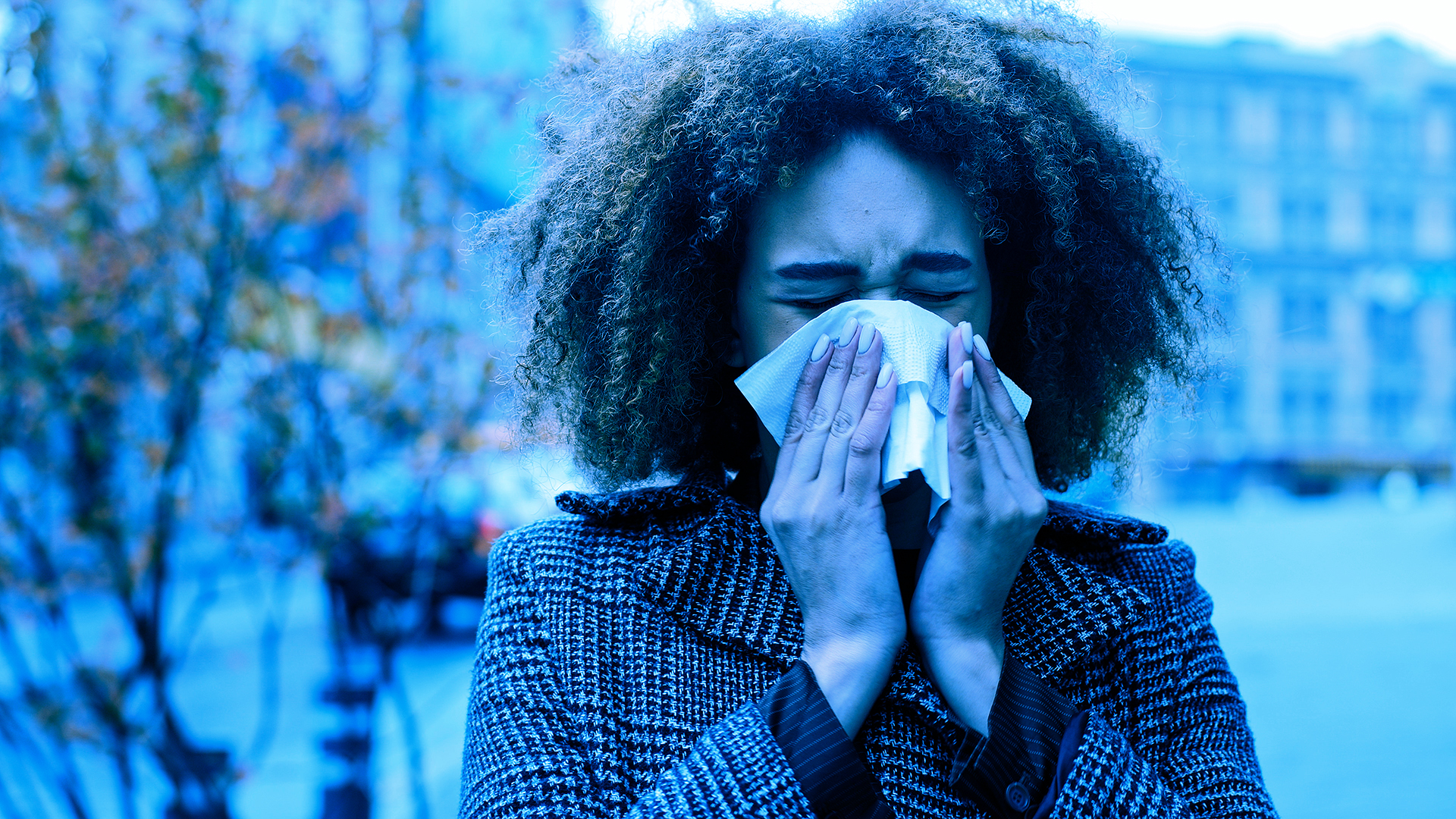 Young woman blowing nose with tissue