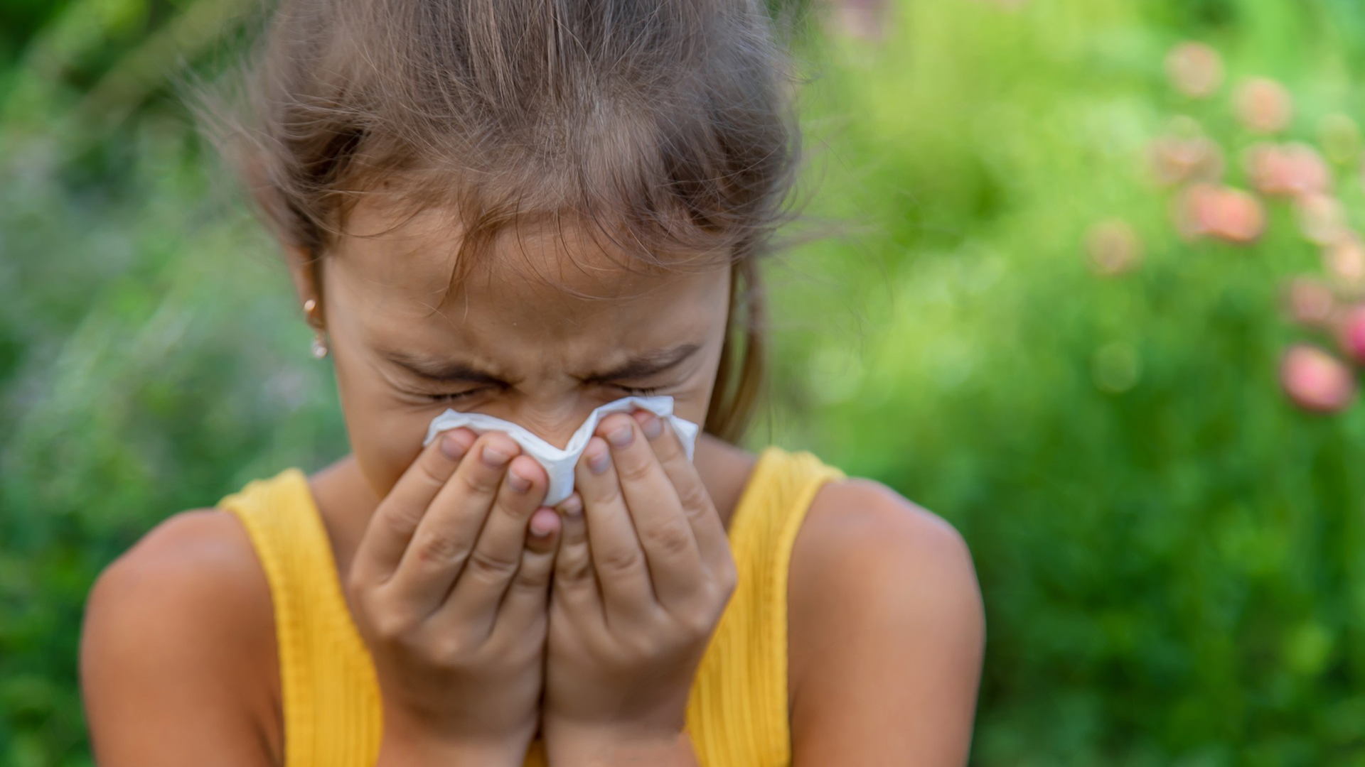 young child wipes her nose in field of blooming flowers